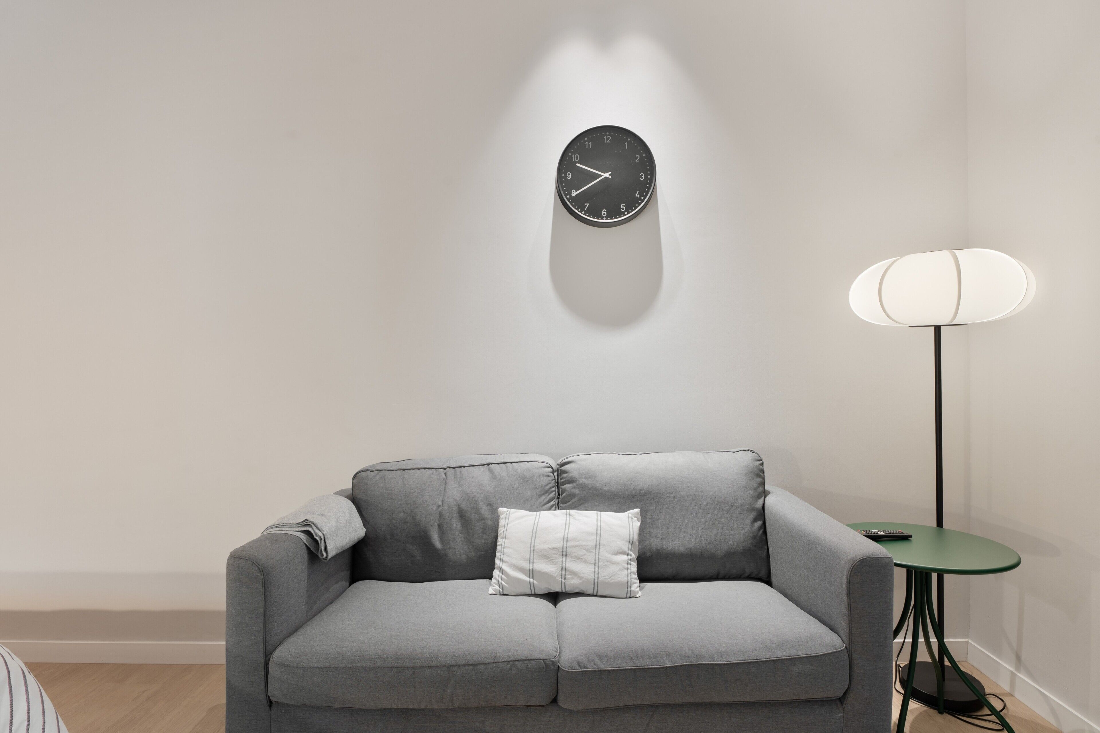 Ein modernes Wohnzimmer mit grauem Sofa, einer Wanduhr, einer Stehlampe und einem kleinen Tisch.