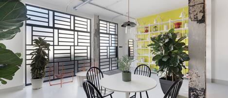 A modern meeting room with a round table, black chairs, potted plants, and a yellow shelving unit.