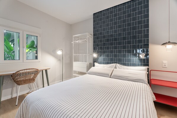 Un dormitorio moderno con cama, escritorio, silla, armario y una ventana grande con vegetación.