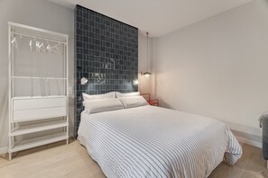 Un dormitorio con una cama, un armario, una mesita de noche y una estantería en la pared.