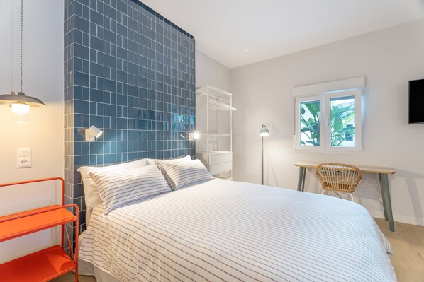 Ein Schlafzimmer mit Bett, Schreibtisch, Stuhl, Regal und Fernseher an der Wand.