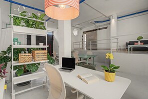 Un espai d'oficina modern amb mobiliari blanc, un escriptori amb un ordinador portàtil, una prestatgeria amb plantes i una planta en test amunt del escriptori.