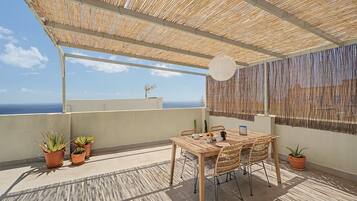 A rooftop terrace with a table and chairs, potted plants, and a view of the sea.