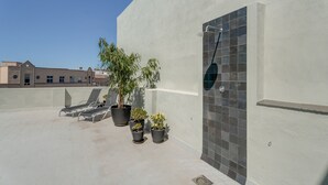 A rooftop terrace with lounge chairs, potted plants, a shower, and a tiled wall.