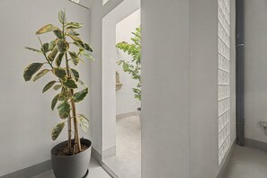 A potted plant in a hallway with white walls and a tiled floor.