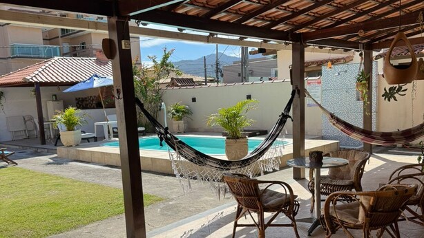 Un patio techado con una hamaca, sillas de mimbre, una piscina y plantas en macetas.
