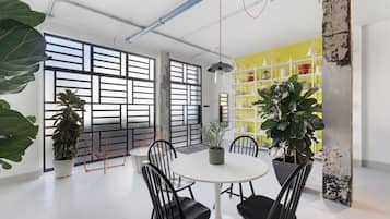 Una sala de reuniones moderna con una mesa redonda, sillas negras, plantas en macetas y un estante amarillo.