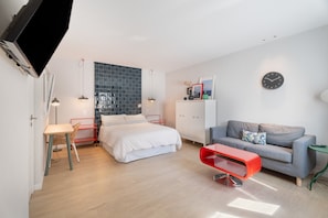 Et moderne soveværelse med en seng, et skrivebord, en rød stol, en grå sofa og et vægur.