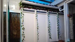 A covered outdoor area with a tiled floor, white doors, and potted plants.