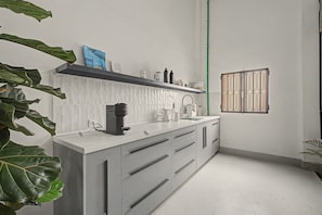 A modern kitchen with white cabinetry, a coffee machine, and a window with bars.