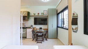 Cocina compacta con comedor, microondas, refrigerador y televisor montado en la pared.