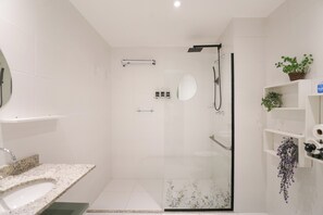 Un baño moderno con ducha de vidrio, lavamanos con encimera de granito y espejo.