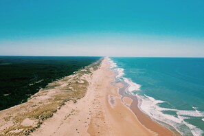 An aerial view of a beach with a long stretch of sand and ocean. - À 100m de la plage | T2 cosy + terrasse & jardin (Carcans)