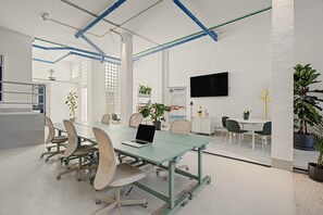 A modern conference room with a glass table, chairs, a laptop, potted plants, and a mounted TV.