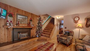 Un salon chaleureux avec une cheminée, un sapin de Noël, un escalier et un canapé confortable.