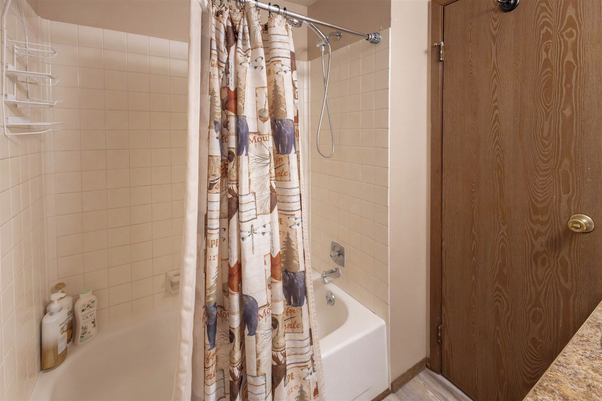 Un baño con bañera, cortina de ducha estampada con motivos de animales y una puerta de madera.