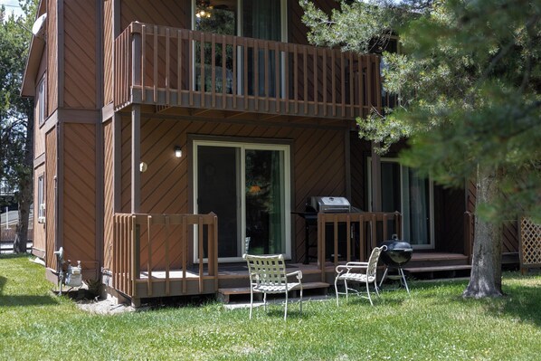 Une cabane en bois avec un balcon, un barbecue et une chaise de jardin.