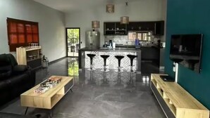 A spacious living area with a black sofa, a wooden coffee table, and a kitchen in the background.