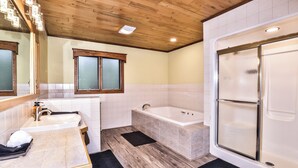 A bathroom with a wooden ceiling, a bathtub, a shower, and a sink with a mirror.