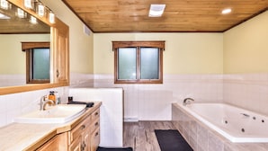 A modern bathroom with a wooden ceiling, a large bathtub, a sink, and a mirror.