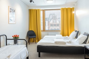 Una habitación de hotel con cama, una silla, una mesita y una ventana con cortinas.