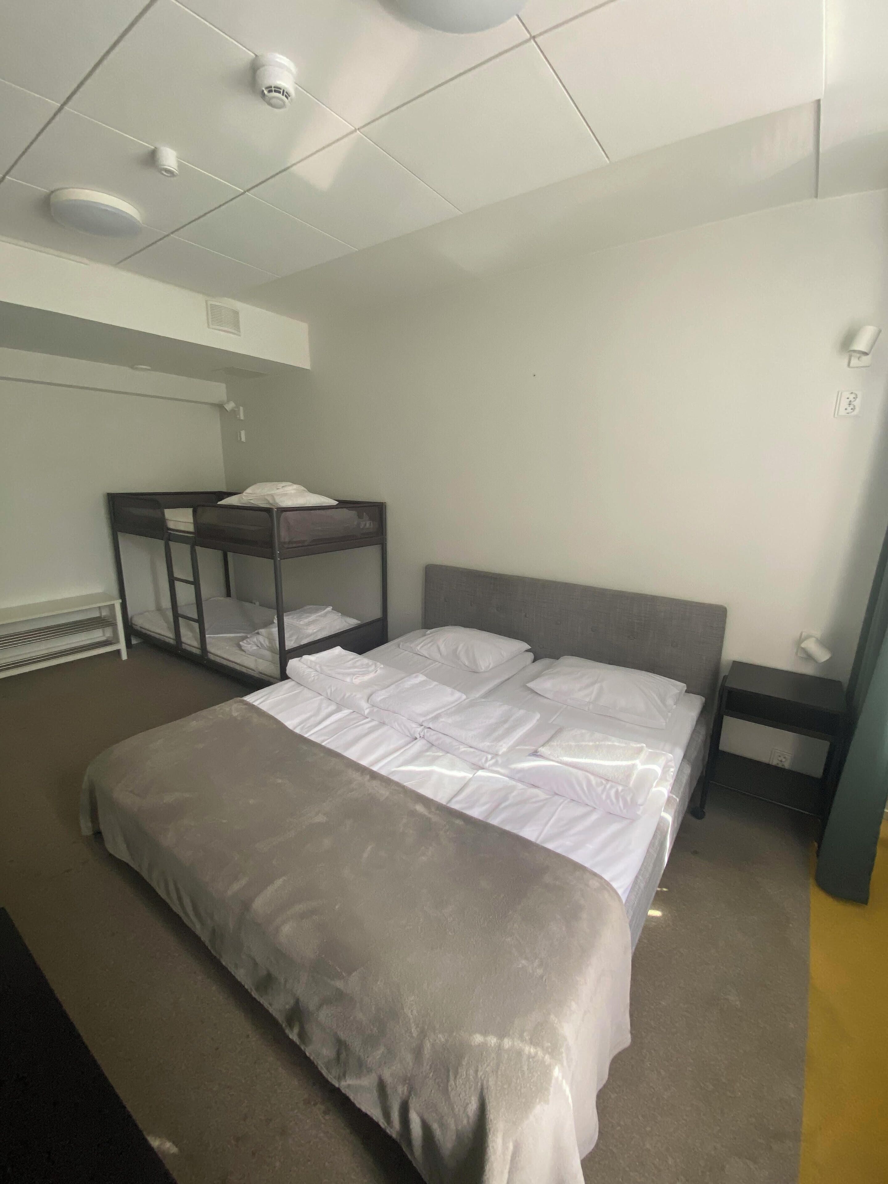 Habitación de hotel con una cama individual, una cama litera, una mesita de noche y una lámpara fijada a la pared.