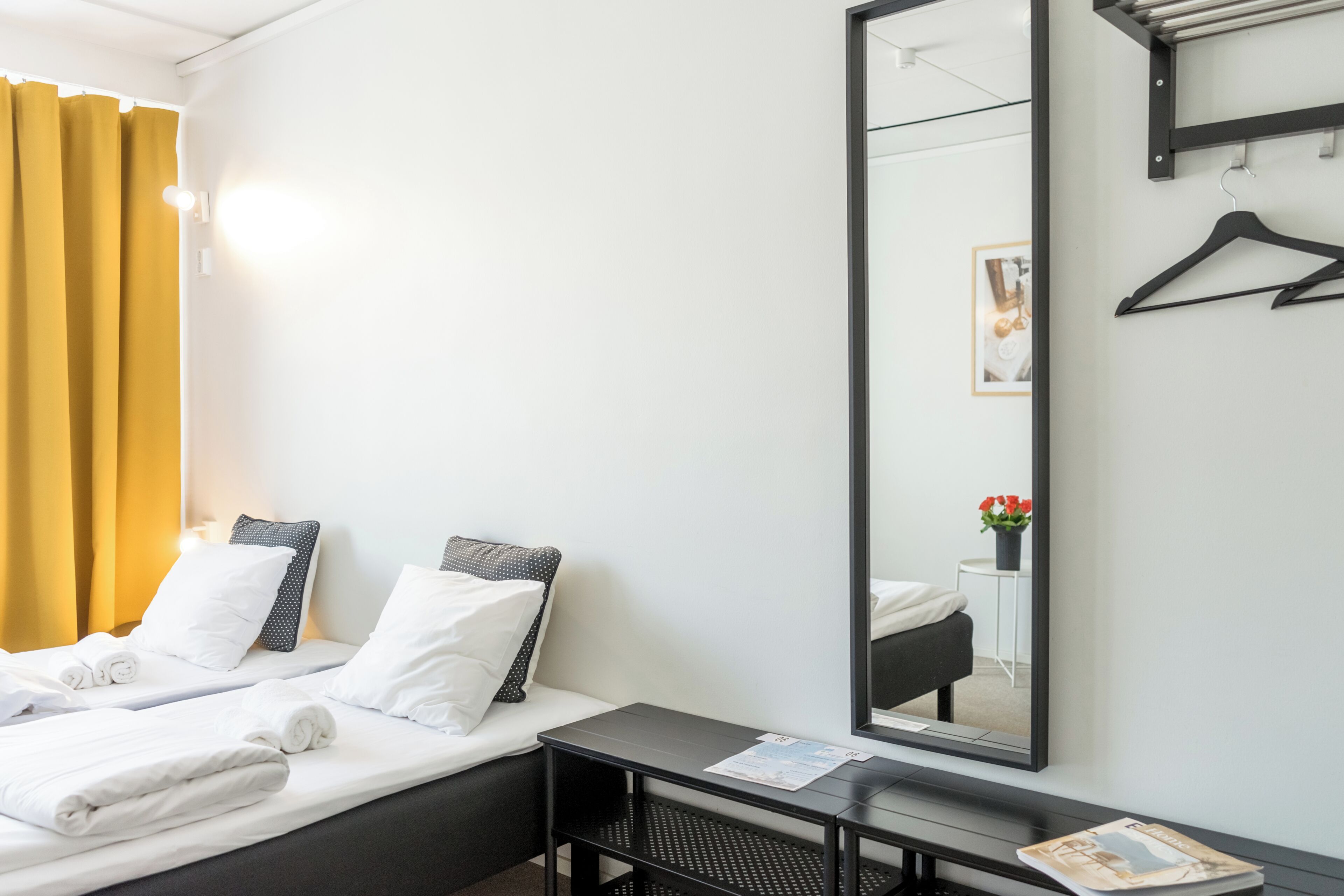 A hotel room with a bed, a bedside table, a mirror, and a window with curtains.