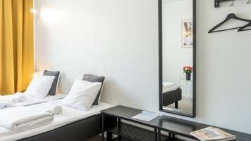 A hotel room with a bed, a bedside table, a mirror, and a window with curtains.