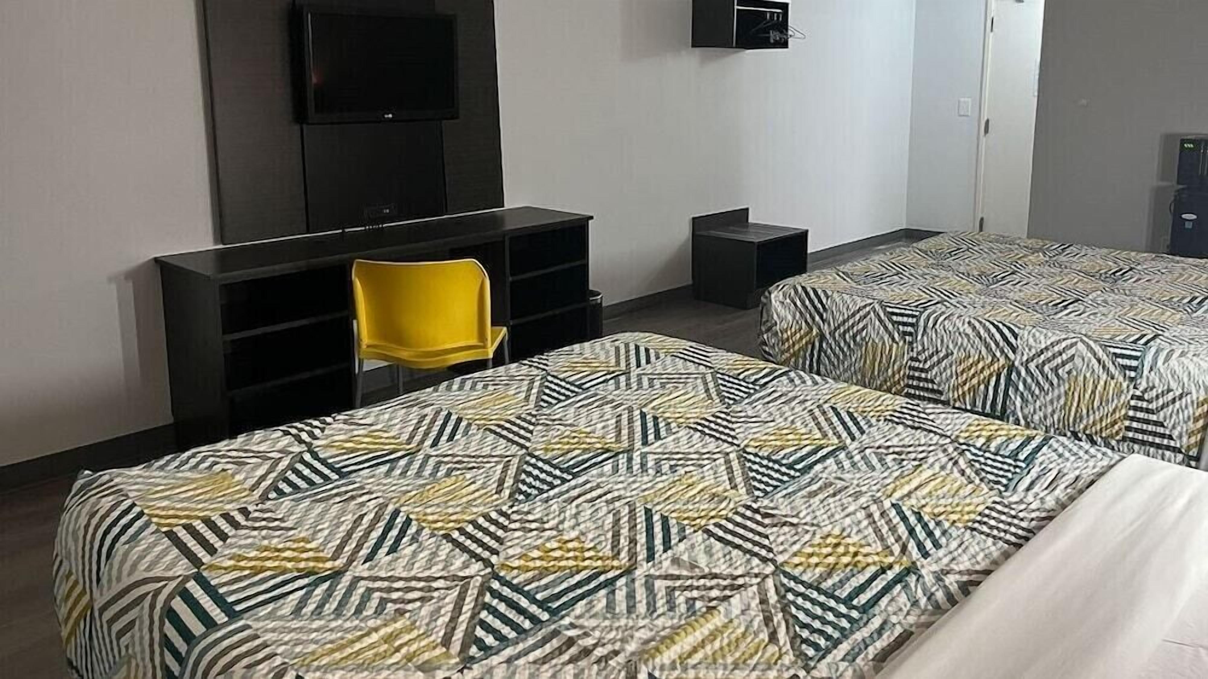 A hotel room with two beds, a TV mounted on the wall, a small desk, and a yellow chair.