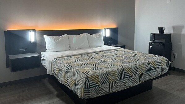 Una habitación de hotel moderna con una cama grande, dos mesitas de noche, una mesita auxiliar, un televisor y un minibar.