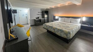 Una habitación de hotel con una cama, un escritorio, una silla, un televisor y una kitchenette.