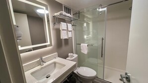 Un baño moderno con cabina de ducha de vidrio, lavabo con espejo y inodoro.