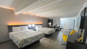 Habitación de hotel con dos camas, un escritorio, una silla y una kitchenette.