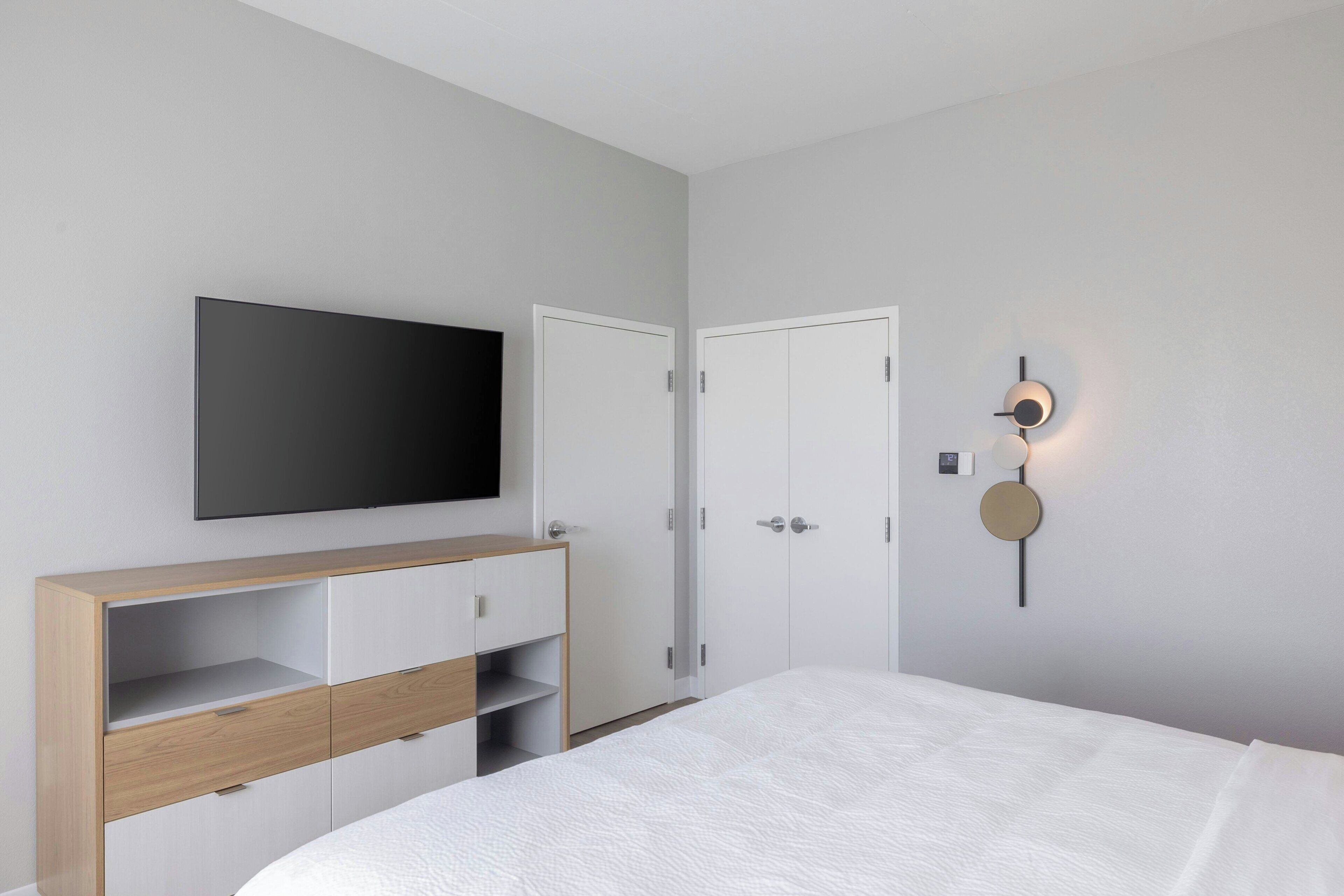 Ein Schlafzimmer mit Bett, Wandfernseher, Kleiderschrank und Wandlampe.