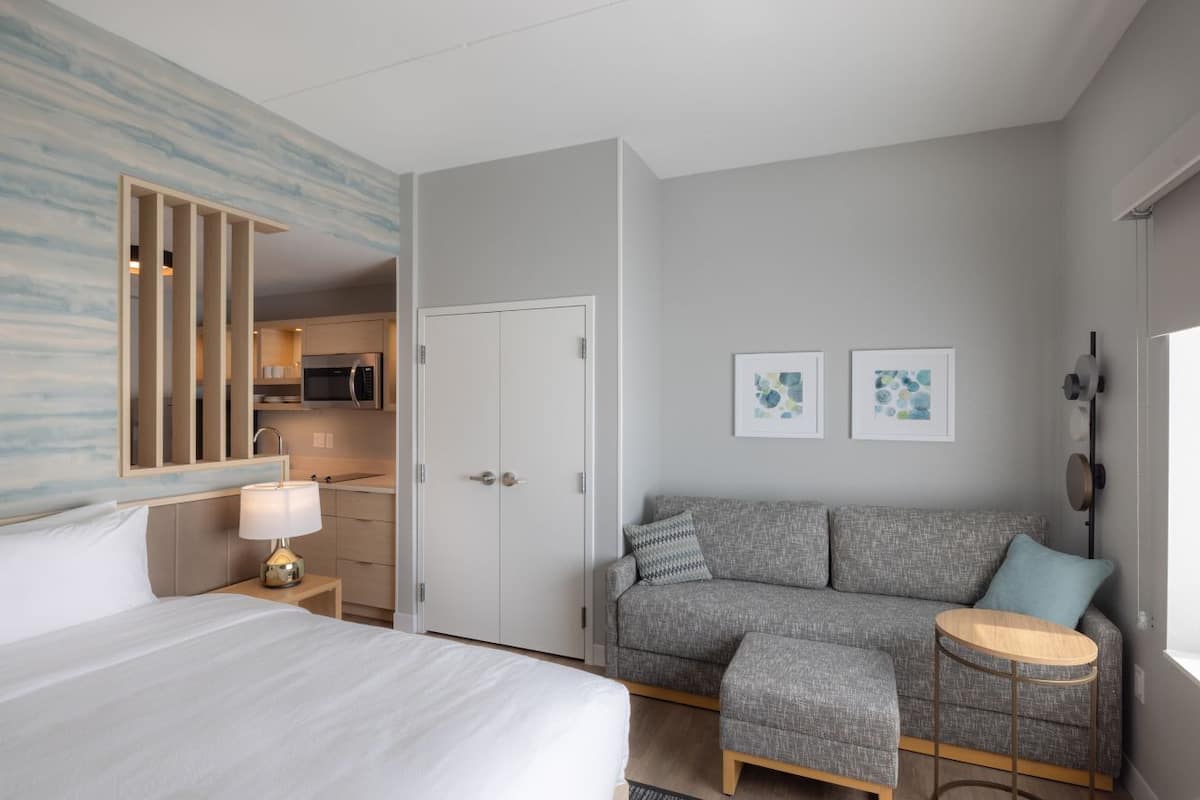 A hotel room with a bed, a sofa, a small round table, a kitchenette, and two framed pictures on the wall.