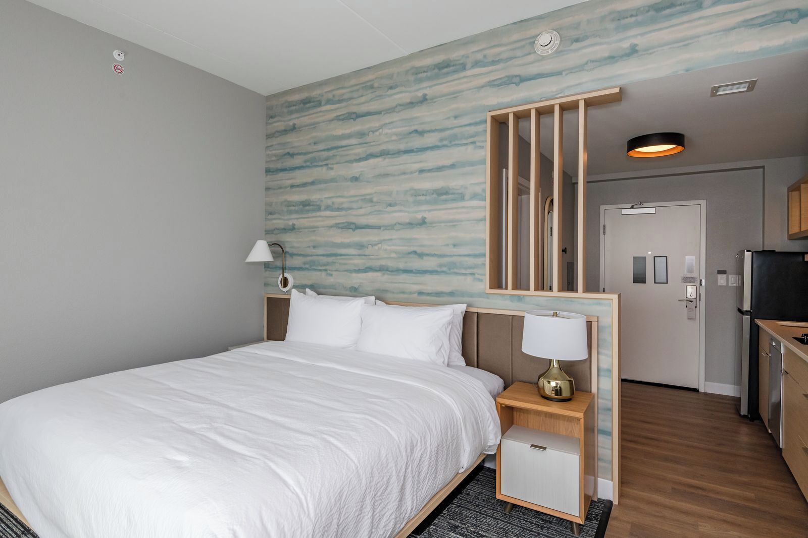 A hotel room with a bed, bedside tables, a desk, a television, and a bathroom door.
