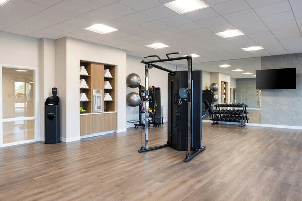 Un gimnasio moderno con equipo de ejercicio, un espejo grande y una televisión.
