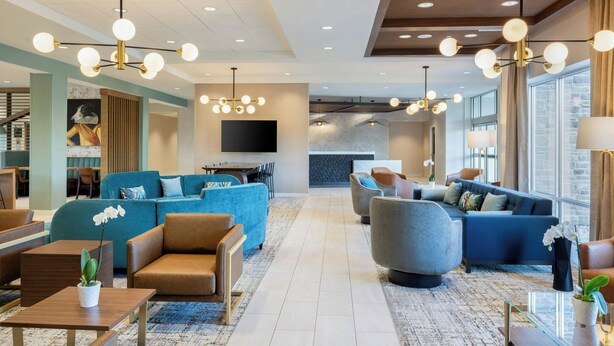 A modern hotel lobby with a mix of seating areas, a flat-screen TV, and a stone accent wall. - Towneplace Suites By Marriott Dayton Beavercreek (Beavercreek)