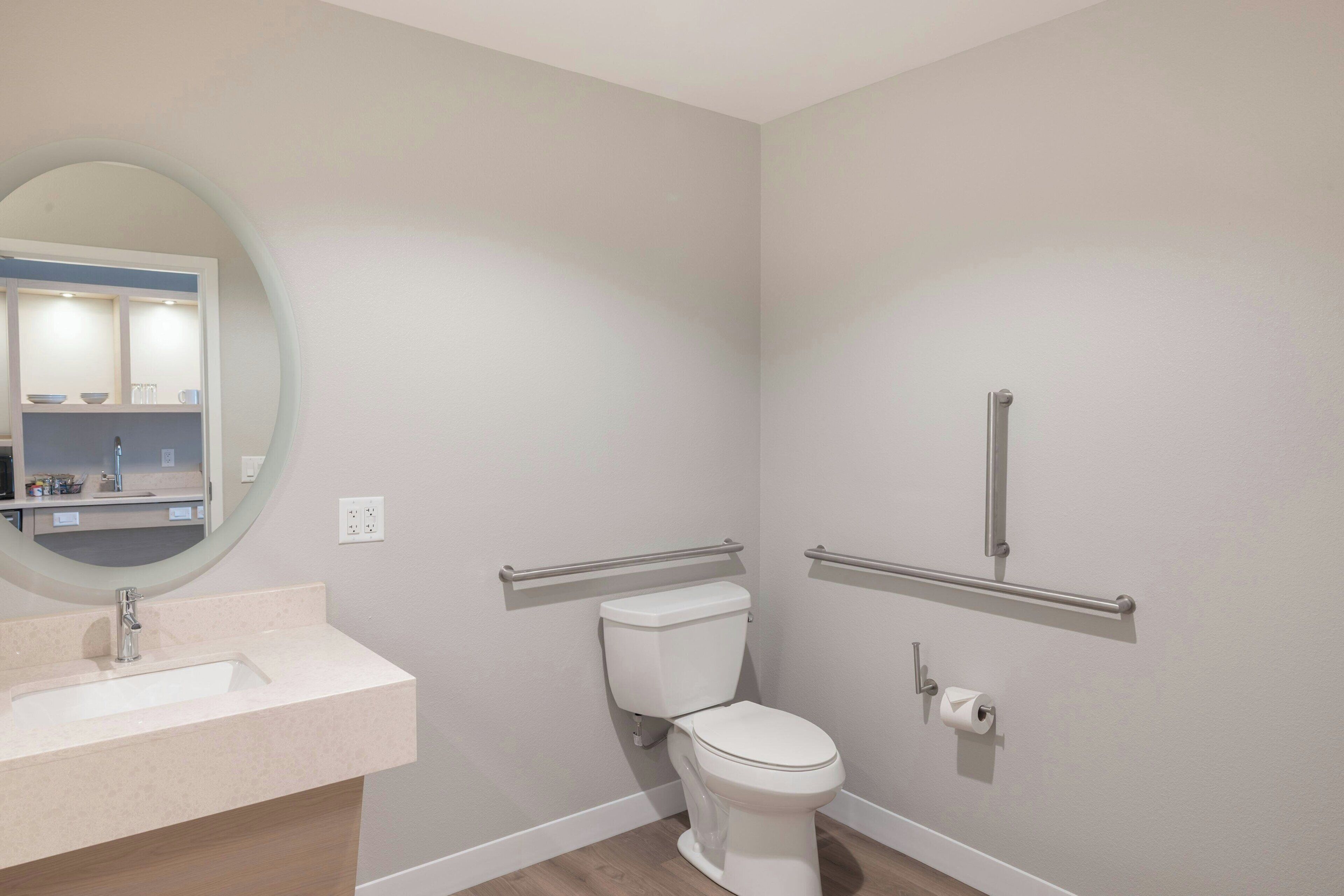 A bathroom with a white toilet, a sink, a mirror, and a handrail.