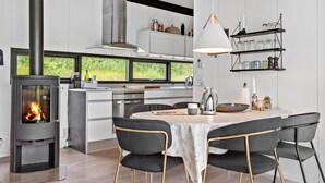 Una cocina moderna con estufa de leña, muebles de cocina blancos y un comedor con mesa y sillas.
