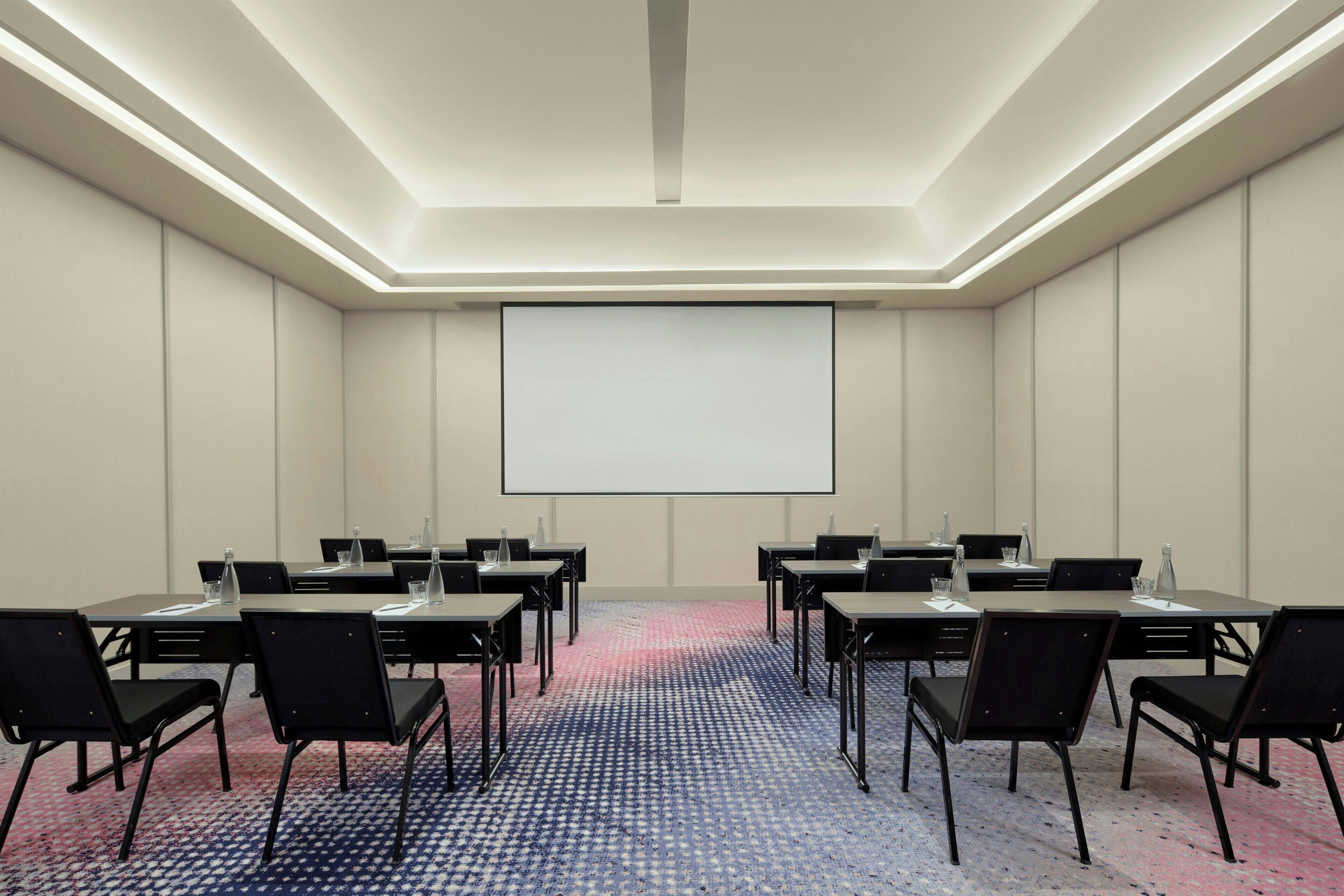 A conference room with a large screen, multiple tables, and chairs arranged for meetings.