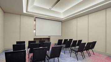 Un salón de conferencias con una pantalla grande, filas de sillas y una alfombra estampada.