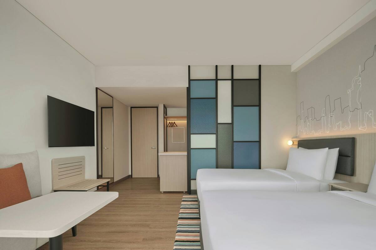 Una habitación de hotel moderna con una cama grande, un escritorio, un televisor de pantalla plana y una obra de arte con vista a la ciudad.