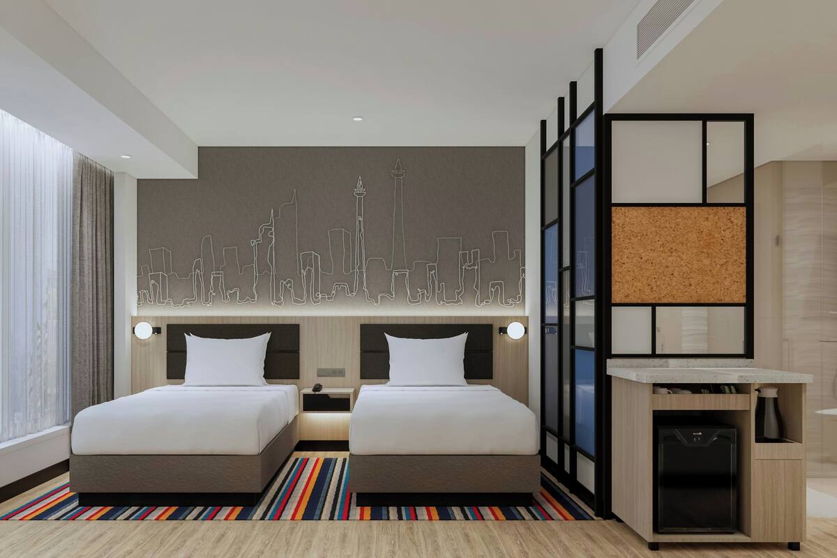 A hotel room with two beds, a city skyline artwork on the wall, a minibar, and a striped rug.