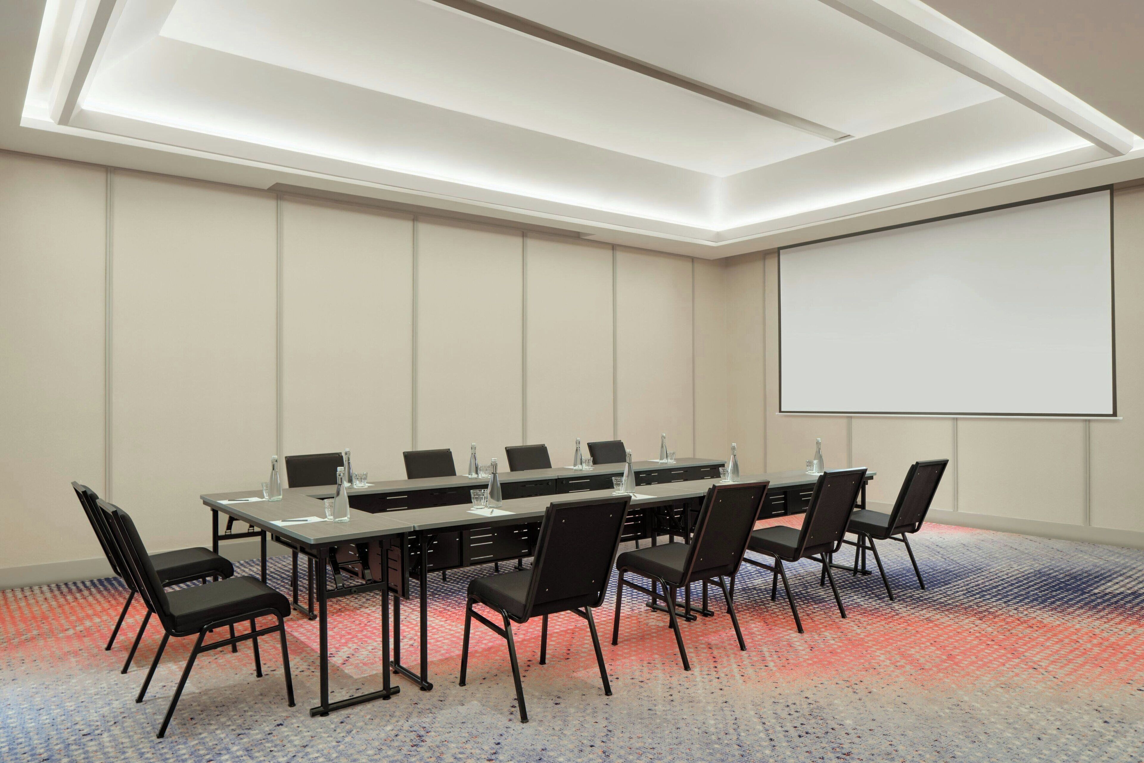Une salle de conférence avec une longue table, des chaises, un écran de projection et un sol recouvert de moquette.