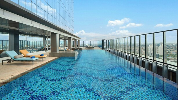 A rooftop infinity pool with lounge chairs and a city view.