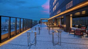 A rooftop terrace with tables and chairs, a city view, and a modern building facade.