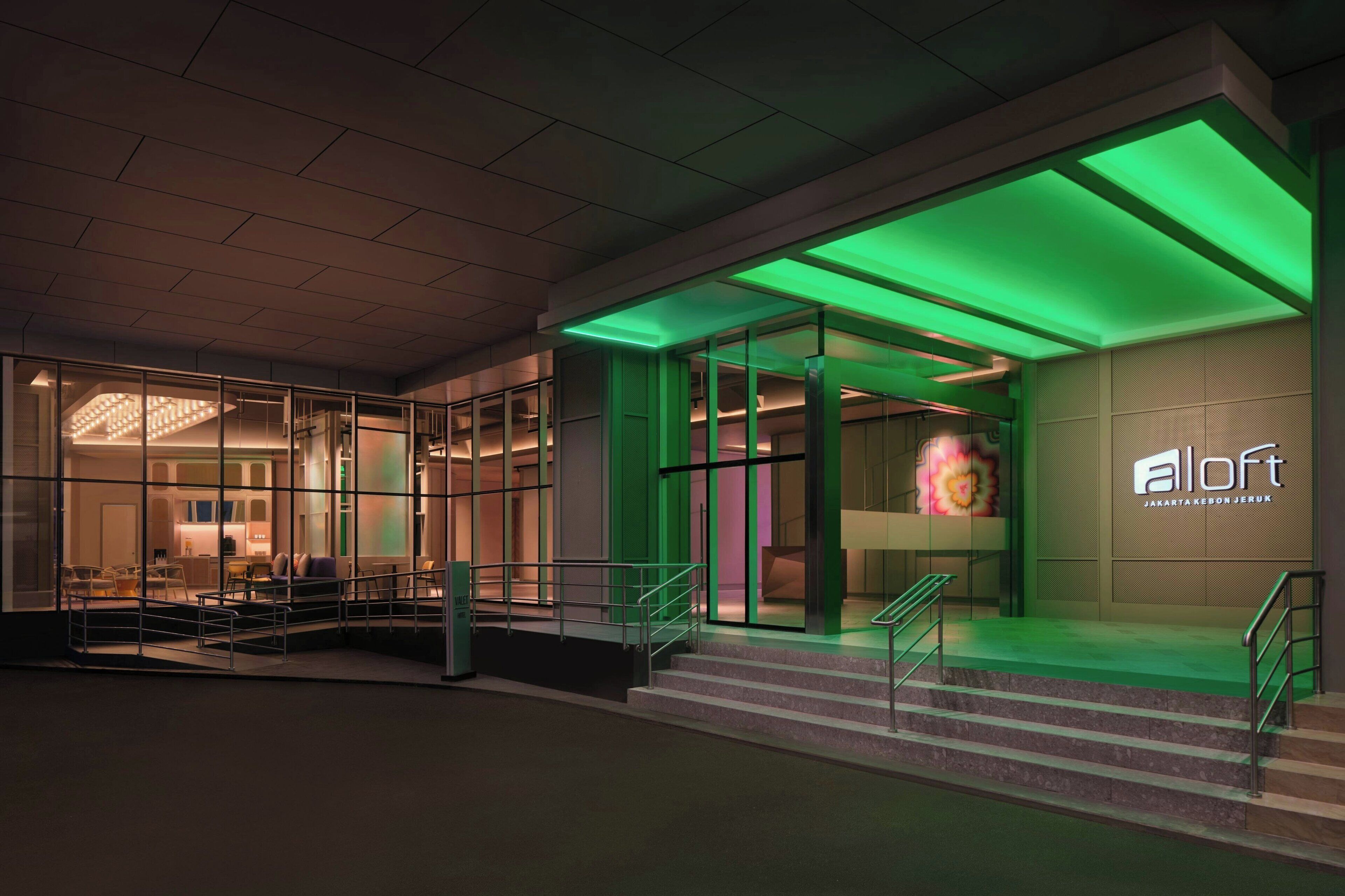 Vestíbulo moderno de hotel con puertas de vidrio, una escalera y ambiente interior iluminado en verde.