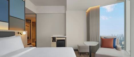 A modern hotel room with a large bed, a seating area, a desk, and a city view.