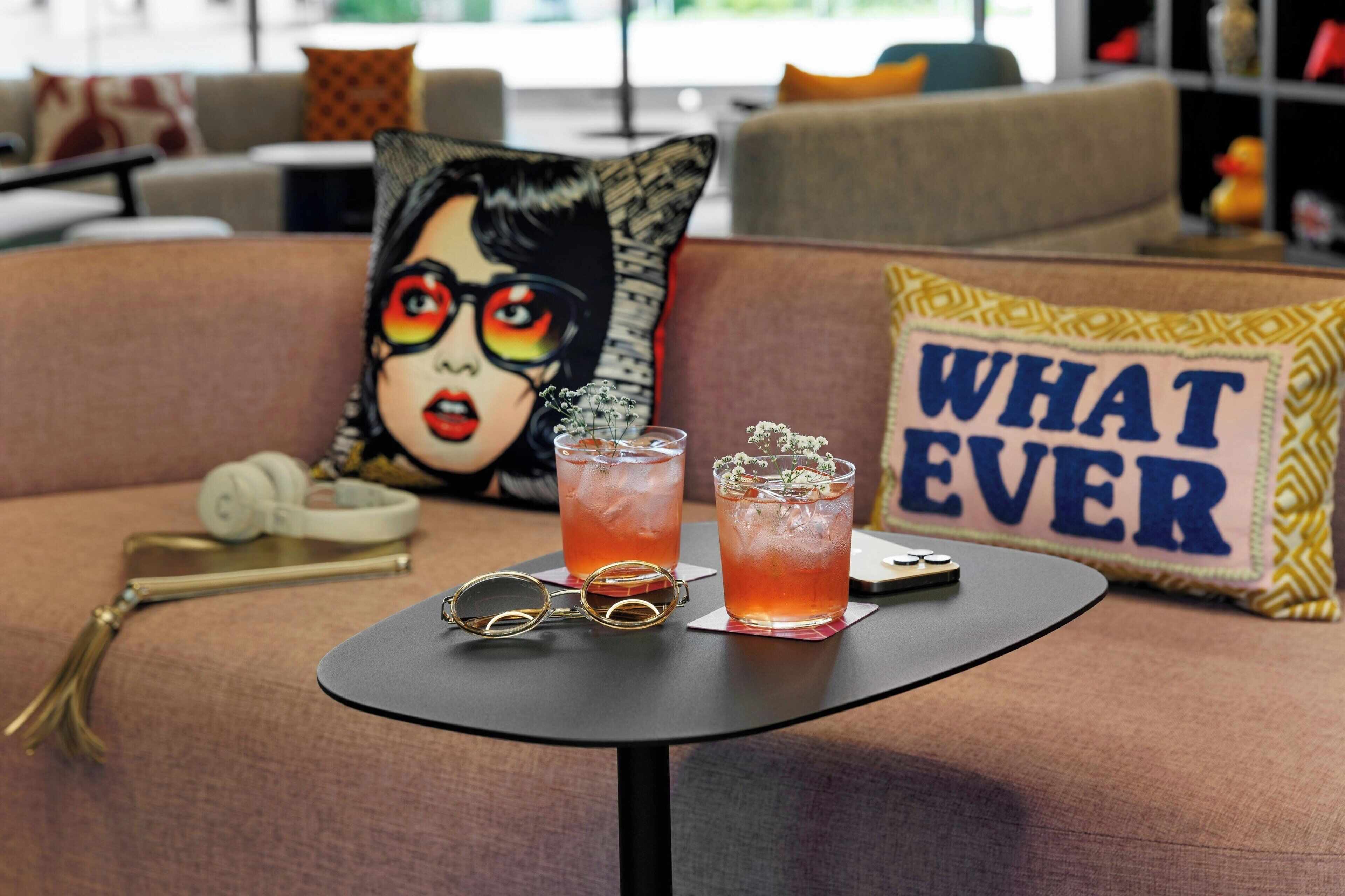 A table with two drinks, a pair of glasses, and a decorative pillow with the text "WHAT EVER" on a couch.